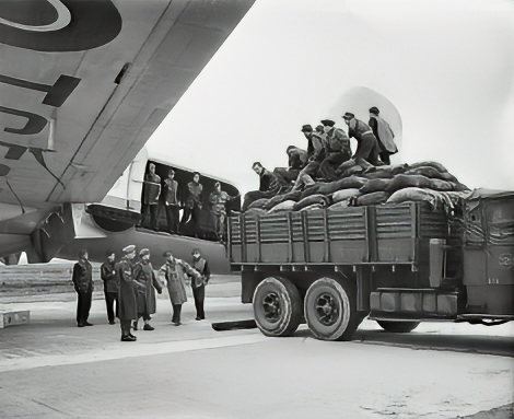 British Army soldiers and German civilians stand by as a truckload of coal is backed up to the loading door of a Handley-Page Hastings at Schleswigland.